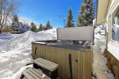 Outdoor hot tub set in snowy surroundings with trees and neighboring homes in the background.