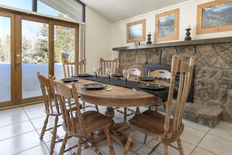 Dining area with wooden table and chairs, stone fireplace, and framed mountain artwork.