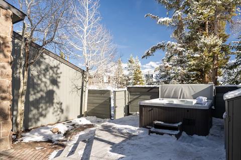 View of mountain home exterior with deck and hot tub on a sunny day. 