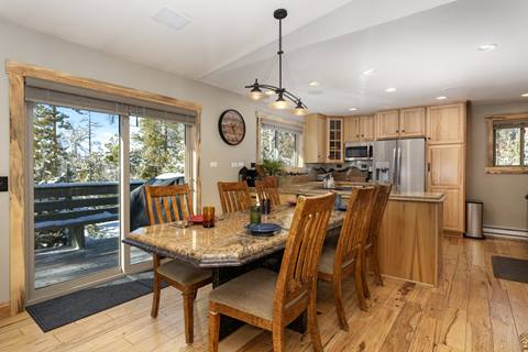 Kitchen with wooden floors, dining room table, and a view onto the balcony that overlooks a mountainous environment. 