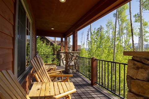 Deck with wooden lounge chairs, a wooden table, stone pillars, and a steel fence with bars. 