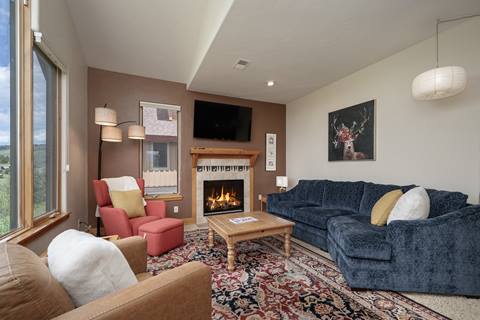 Cozy living room with a red armchair, blue sectional sofa, and a fireplace beneath a mounted TV.