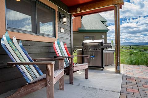 Patio with Adirondack chairs made from skis and a stainless steel gas grill, overlooking mountain views.