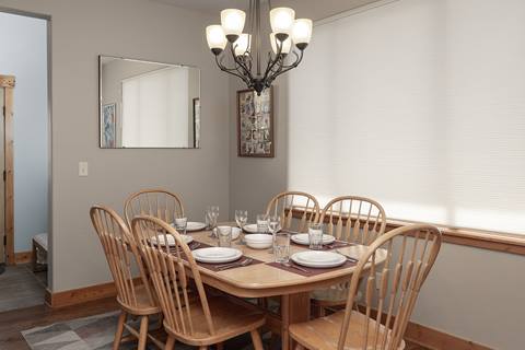Wooden dining table set for six with matching chairs, chandelier lighting, and a wall mirror.