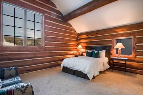 Cozy bedroom with log walls, a bed with white bedding, two bedside tables with lamps, and a window with mountain views.