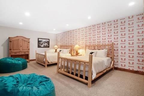 Spacious bedroom with two log-frame full beds, moose-print wallpaper, teal bean bags, and rustic armoire.