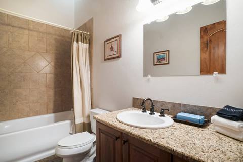 Bathroom with granite countertop vanity, white sink, tiled shower-tub combo with curtain, and framed artwork on the wall.