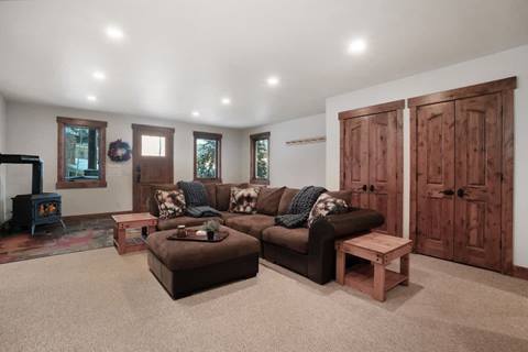 Spacious living room with a large brown sectional sofa, wood stove, rustic doors, and neutral carpet flooring.