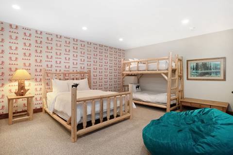 Bedroom with log-frame bunk beds, full bed, moose-print wallpaper, and teal bean bag chair.
