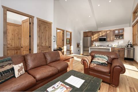 Open living space with brown leather seating, rustic wood doors, and a view into the modern kitchen.