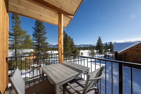 Balcony with a small outdoor dining table overlooking snow-covered trees and mountains.