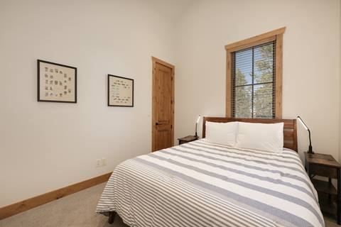Bedroom with striped bedding, wooden bed frame, and window views of pine trees.