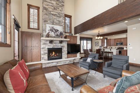 Spacious living room with vaulted ceilings, stone fireplace, and open floor plan leading to dining and kitchen areas.