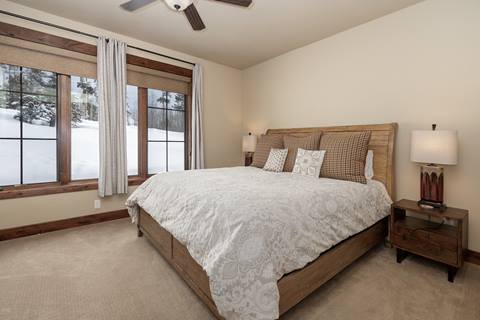 Bedroom with king bed, neutral bedding, and large windows overlooking snow-covered trees.