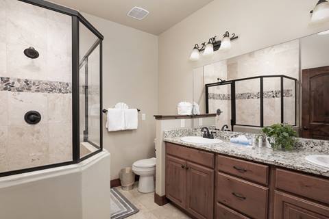 Bathroom with double sinks, granite countertops, and large walk-in glass shower.