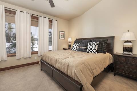 Bedroom with king bed, beige bedding, and large windows with curtain panels.