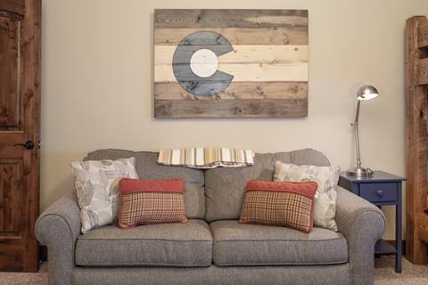 Cozy loveseat with plaid and floral pillows under a rustic Colorado state flag wall art.