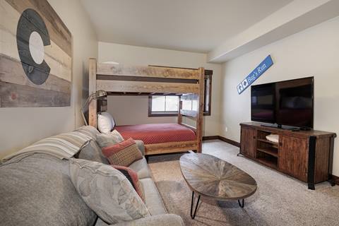 Bunk room with a full-size bed on the bottom, couch, TV, and rustic ski-themed wall décor.