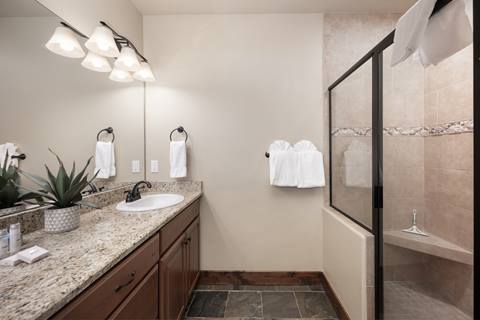 Bathroom with granite countertop, single vanity, and glass-enclosed shower with tiled bench.