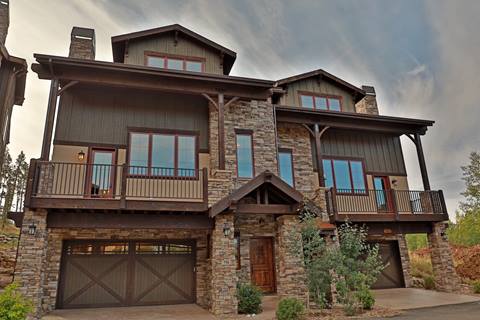 Exterior view of Mountain Terrace townhomes in summer with stone and wood façade, multiple balconies, and two-car garage.