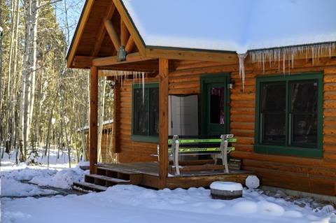 Exterior view of log cabin in winter with front porch and snow-covered roof.