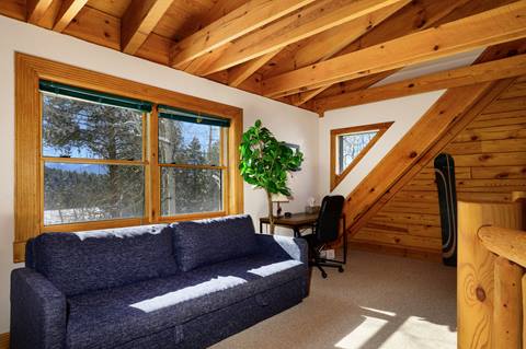Loft area with sofa, workstation, and large window with forest view.