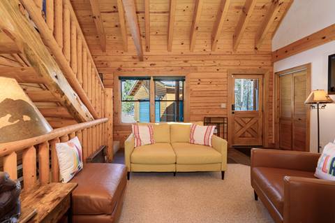 Living room with wood-paneled walls, yellow loveseat, leather chairs, and vaulted ceiling.