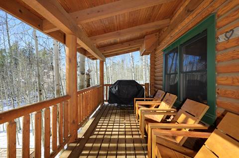Covered deck with gas grill and wooden chairs overlooking aspen trees.