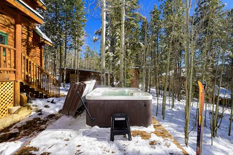 Outdoor hot tub on a snowy patio surrounded by forest.
