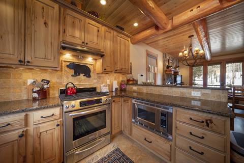 Range with stone/tiles and bear motif backsplash, built-in microwave, granite counters, exposed logs.