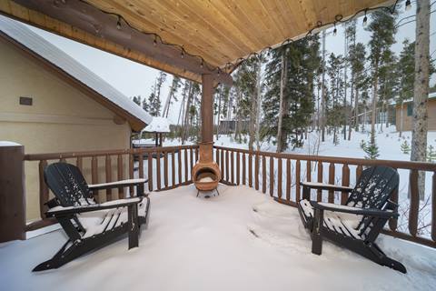 Chiminea and two Adirondack chairs on a snow-dusted porch facing the trees.