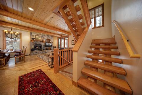 Log staircase off the kitchen leading to the living area with stone hearth in view.