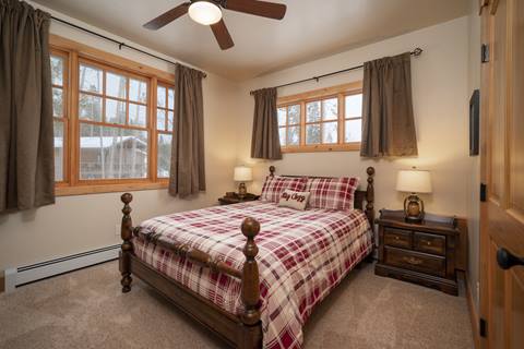 Cozy queen bed with “Stay Cozy” pillow, dual nightstands, and multiple windows.