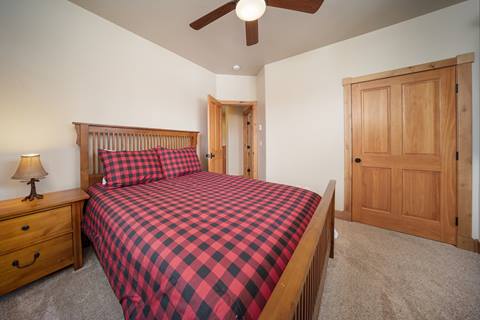 Queen bed with red/black check duvet, nightstand, ceiling fan, and paneled door.