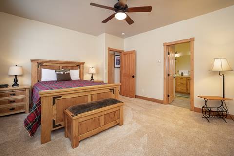 Spacious king bedroom with plaid bedding, wood furniture, and a ceiling fan, leading into an en suite bathroom.