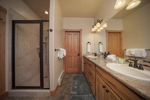 En suite bathroom featuring a walk-in shower, dual sinks, and granite countertops with wood cabinetry.