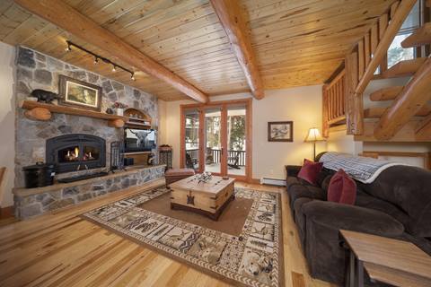 Stone fireplace with gas insert, log beams, and glass doors opening to the covered deck; plush sofa seating.