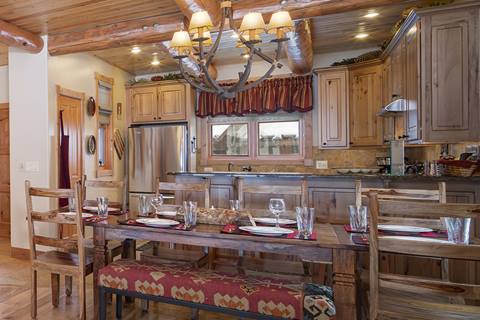 Rustic table for eight with antler chandelier; stainless appliances and breakfast bar behind.