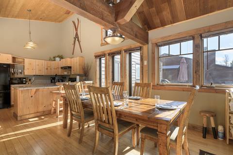 Dining area with rustic wood table, six chairs, and vaulted ceilings, adjacent to the kitchen.