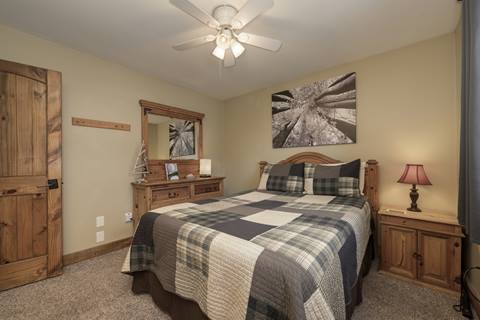 Bedroom with plaid quilt, wood furniture, and warm accent lighting.