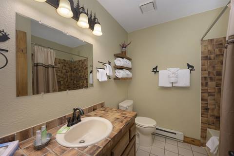 Full bathroom with tiled countertop, sink, and tub-shower combo featuring brown patterned tiles.