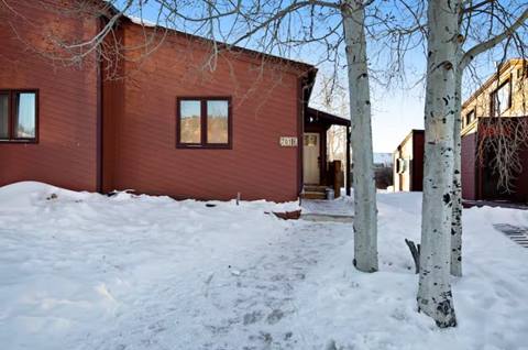 Front exterior of Quail property in winter with red siding, snow on the ground, and trees by the entryway.