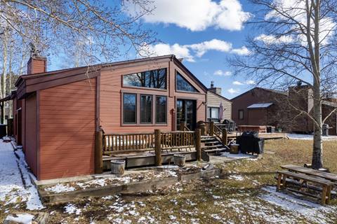 Rear exterior of Quail property with red siding, deck, BBQ grill, and picnic table in snowy backyard.
