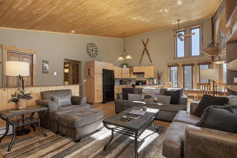 Open-concept living room with plush seating, vaulted wood ceilings, and direct view of the kitchen.