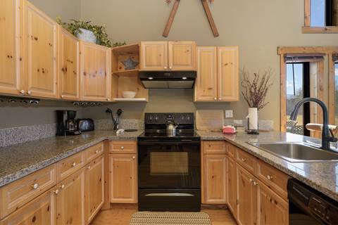 Kitchen detail featuring wood cabinetry, black stove, granite counters, and rustic décor.