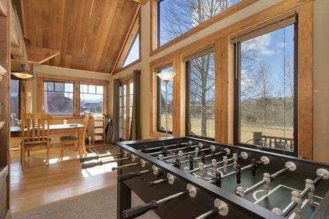 Dining nook and game area with foosball table, wood-paneled walls, and large picture windows.