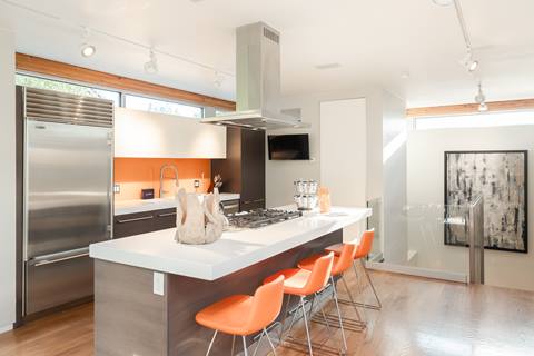 Contemporary kitchen with white island, orange barstools, stainless steel appliances, and modern lighting.