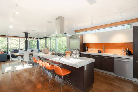 Open kitchen and dining space with large island, orange backsplash, barstools, and floor-to-ceiling windows.