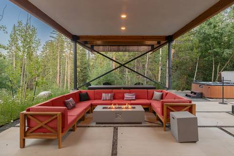 Outdoor covered lounge with red sectional seating, fire pit, and hot tub in the background.