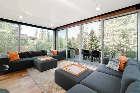 Living room with dark sectional sofas, orange pillows, and sliding glass doors to the deck.